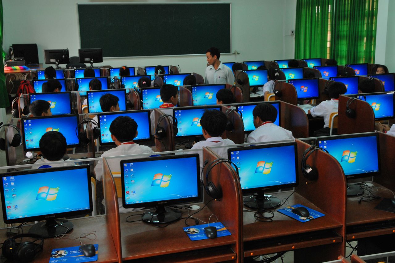 portfolio-02 Students learning in a computer lab with multiple monitors and a teacher instructing.