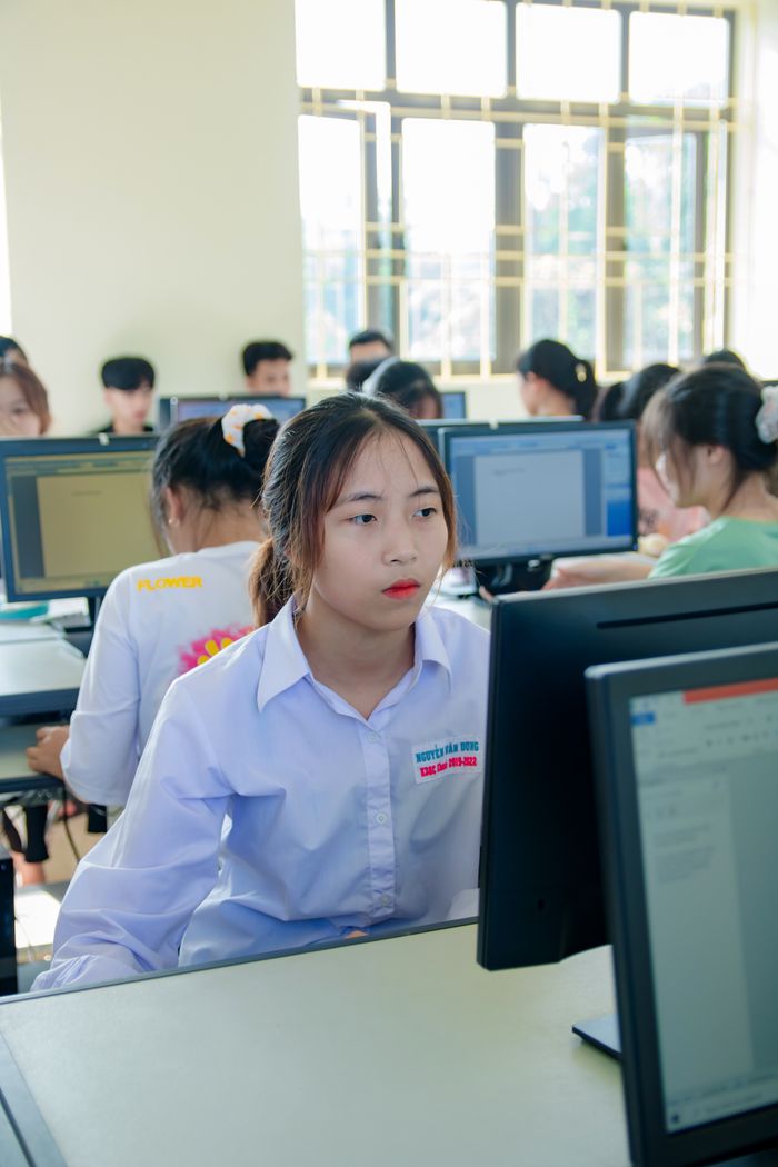 about-img Asian woman focused on computer screen in a modern office with colleagues.