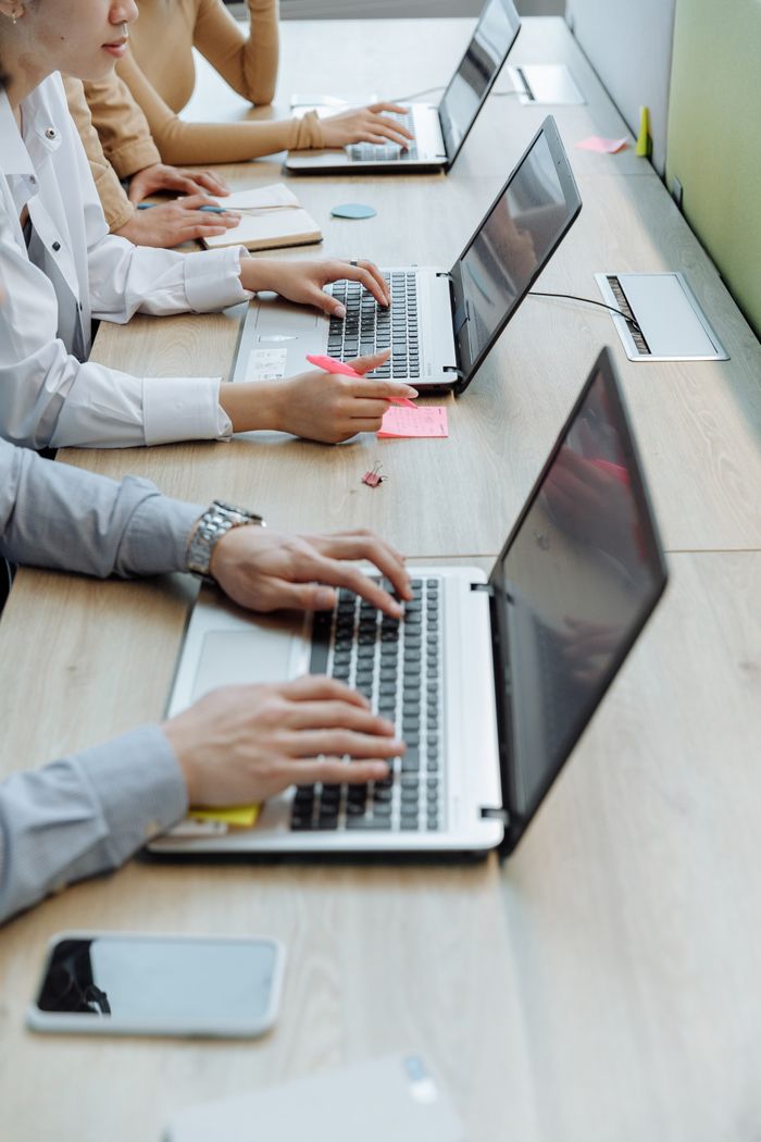 portfolio-04 Group of office workers typing on laptops at a shared workspace desk.